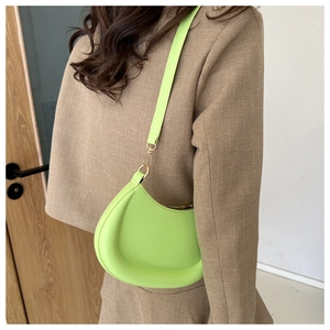 Detail of neon green crescent bag on a khaki blazer, focusing on the curved silhouette