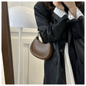 Brown crescent shoulder bag with gold hardware worn by model in stylish leather jacket