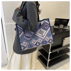 Model wearing a large canvas tote bag with blue ethnic geometric patterns and webbing handles