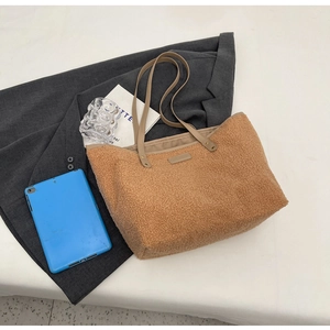 Flat lay of brown plush tote bag with leather straps on dark blazer and white background