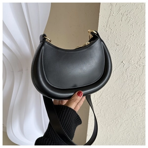 Detail view of a black crescent hobo bag with gold hardware held by a person