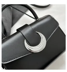 Detailed view of black leather crossbody bag featuring a silver crescent moon buckle