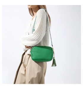 Detail of green leather camera bag with tassel charm and patterned wide strap