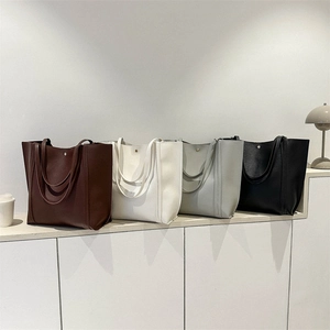 Große Leder-Tote-Taschen in vier Farben auf einem minimalistischen weißen Display-Ständer