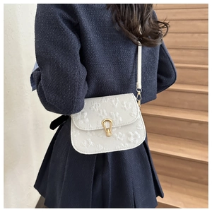 Detail of floral embroidery on cream crossbody bag with golden U-shaped metal clasp