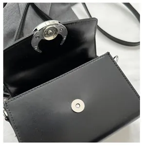 Detail of the silver crescent moon magnetic buckle on a black leather crossbody bag