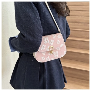 Detail of pink floral embroidered crossbody bag with gold buckle on blue tweed jacket