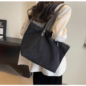 Detail of black fleece tote bag with leather straps worn by model in beige suit