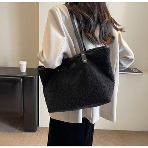 Plush black tote bag with fashion tag and golden rivets worn by model in a modern room