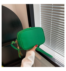 Detail of green lychee-textured crossbody bag with golden zipper and leather tassel charm