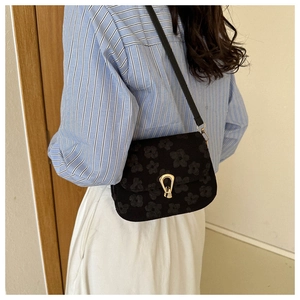 Detail of black crossbody bag with embossed floral pattern and gold U-shaped metal lock