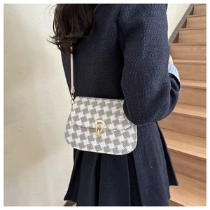 Detail view of plaid crossbody bag featuring a gold horseshoe buckle on wooden stairs