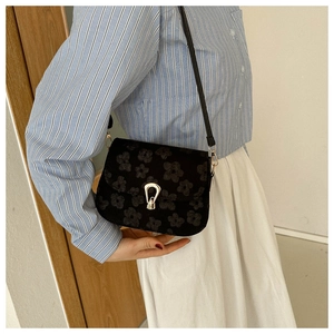 Detail of black floral jacquard shoulder bag with golden horseshoe clasp on model
