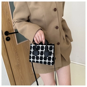 Detail view of mini black and white plaid tweed crossbody bag styled with a beige suit