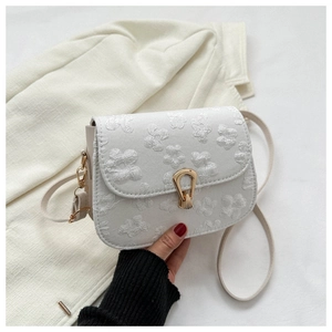 Detail of white crossbody bag featuring 3D floral texture and elegant gold clasp