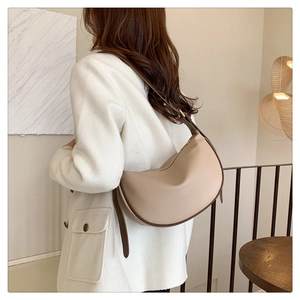 Model wearing a minimalist cream half-moon hobo bag with brown shoulder strap details