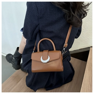 Brown leather crossbody bag with silver crescent moon buckle on a wooden step