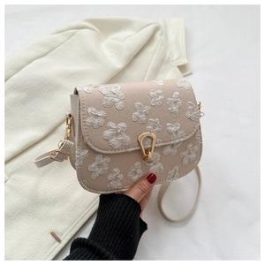 Detail of beige shoulder bag with floral embossed texture and gold trapezoid lock
