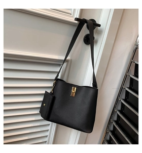 Detail of minimalist black leather bucket bag featuring gold clasp and mini coin purse charm