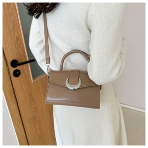 Detail of a brown leather crossbody bag with silver crescent buckle and round handle