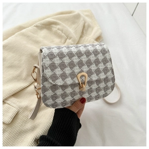 Detail of grey houndstooth fabric texture and unique gold metal buckle on a small square bag