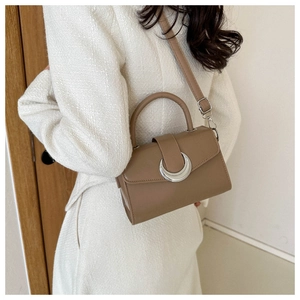 Close-up of tan leather crossbody bag with a large silver crescent buckle on white jacket