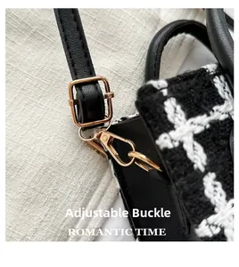 Detail of adjustable gold metal buckle on a black leather strap of a plaid woven bag