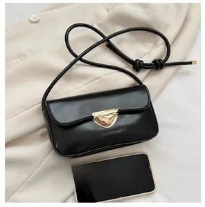 Close-up of black leather crossbody bag with gold triangle buckle and phone for size