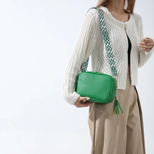 Green leather camera bag with a wide woven geometric strap and long tassel detail
