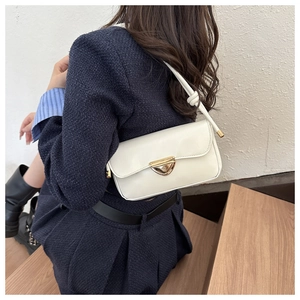 Detail of cream white shoulder bag with gold heart clasp and thin strap worn by model