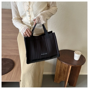 Detail of black quilted tote bag with white fashion tag and soft vertical stitching