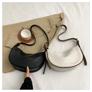 Detail of minimalist half-moon shoulder bags in black and beige PU leather over a textured bed