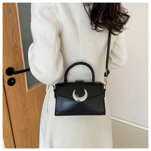 Detail of black crossbody bag with silver crescent moon buckle on tweed jacket background