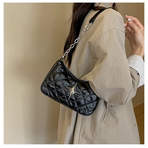 Detail of black quilted leather shoulder bag with silver star logo worn on khaki coat