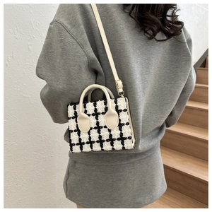 Detail of checkered tweed crossbody bag with cream leather handle and metal hardware