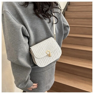 Detail of white pleated crossbody bag featuring a golden U-shaped metallic twist lock