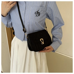 Detail of black pleated crossbody bag with a golden horseshoe buckle on a striped shirt