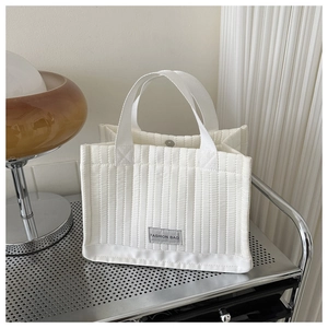 Detail shot of white quilted tote bag featuring metal magnetic closure and fashion textile label