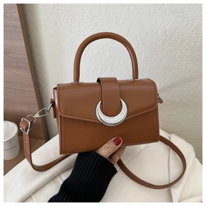 Detail of a brown leather crossbody bag featuring a half-moon silver metal buckle
