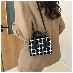Detail of checkered tweed handbag with leather strap on a model wearing brown blazer