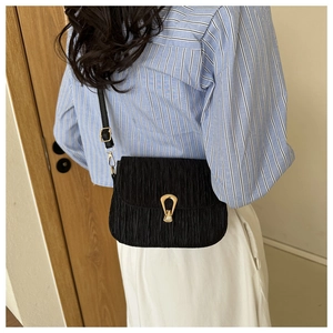 Detail of black pleated crossbody bag featuring a distinctive gold U-shaped metal buckle