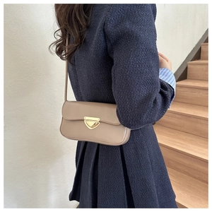 Detail of khaki leather shoulder bag with a gold triangular lock on navy coat