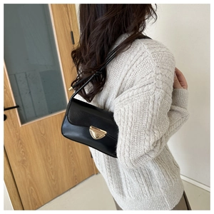 Detail of black leather shoulder bag with gold triangular clasp on beige sweater