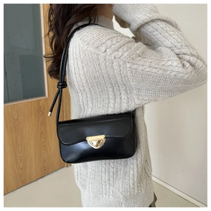 Side view of black leather underarm bag with gold triangle clasp worn by a model