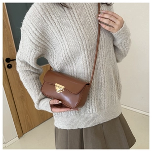 Detail of a brown shoulder bag featuring a gold triangular metal buckle and smooth leather