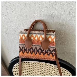 Detail of bohemian woven crossbody bag with orange geometric patterns on a wooden chair