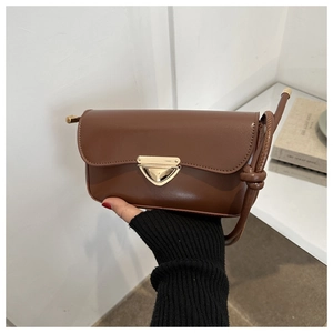 Detail of a brown leather shoulder bag featuring a unique gold triangle buckle closure