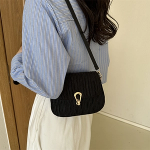 Elegant black pleated shoulder bag with gold clasp shown on model with striped shirt