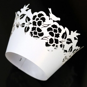 Detailed close-up of white laser-cut cupcake wrapper featuring floral and bird motifs