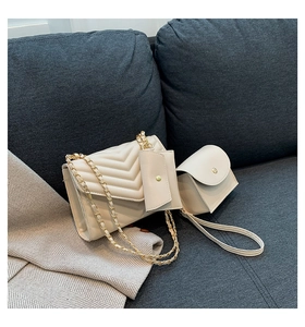 Detailed view of beige V-quilted faux leather bag set with gold chain on a grey sofa